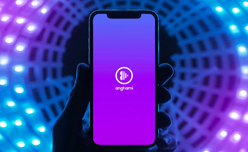 Hand set against purple lights holding mobile phone displaying Anghami