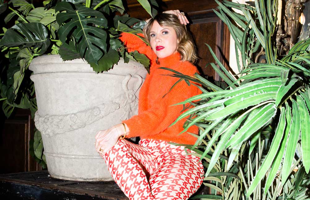 Sarah Neufeld in orange jumper between large indoor plants